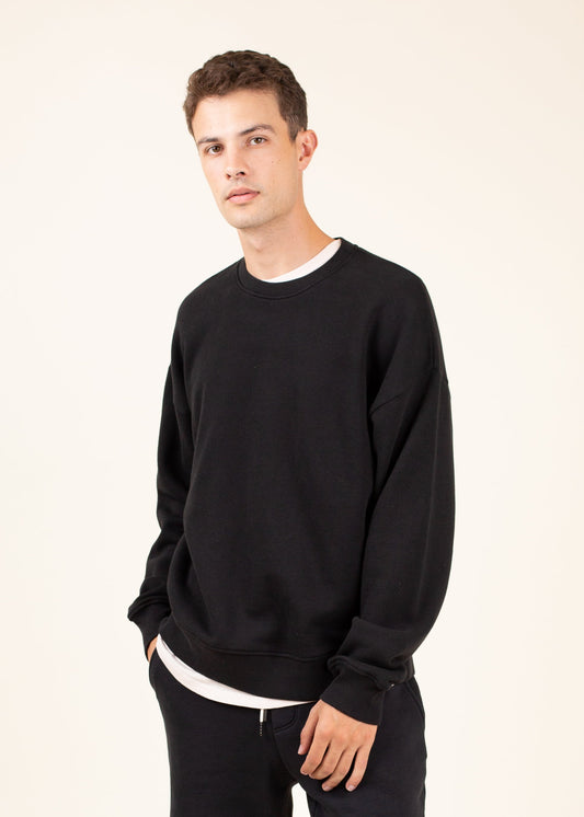 Man modeling minimalist black crewneck sweatshirt and pants, MANN men's fashion lifestyle