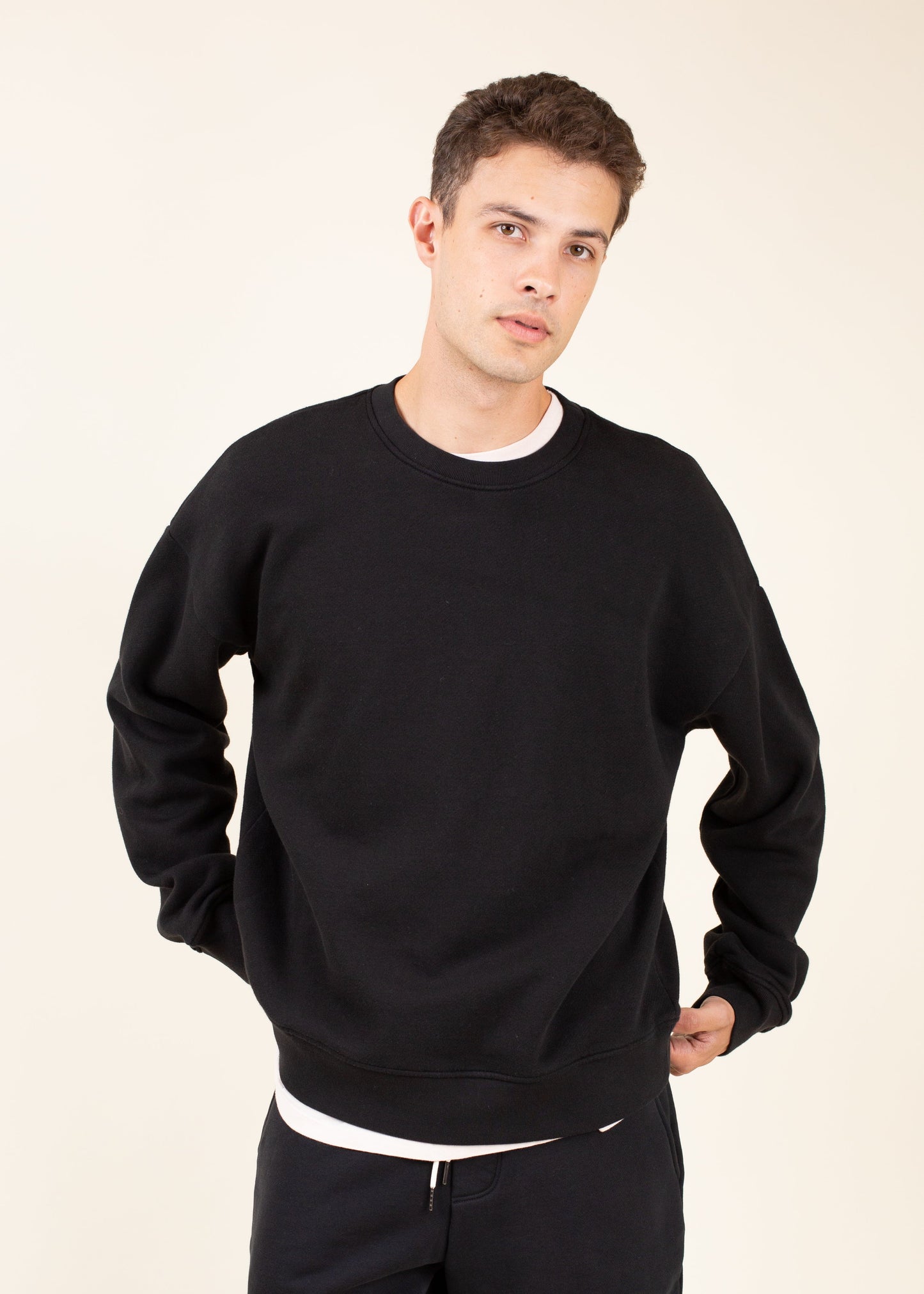 Man wearing black crewneck sweatshirt and joggers, casual men's fashion on neutral background