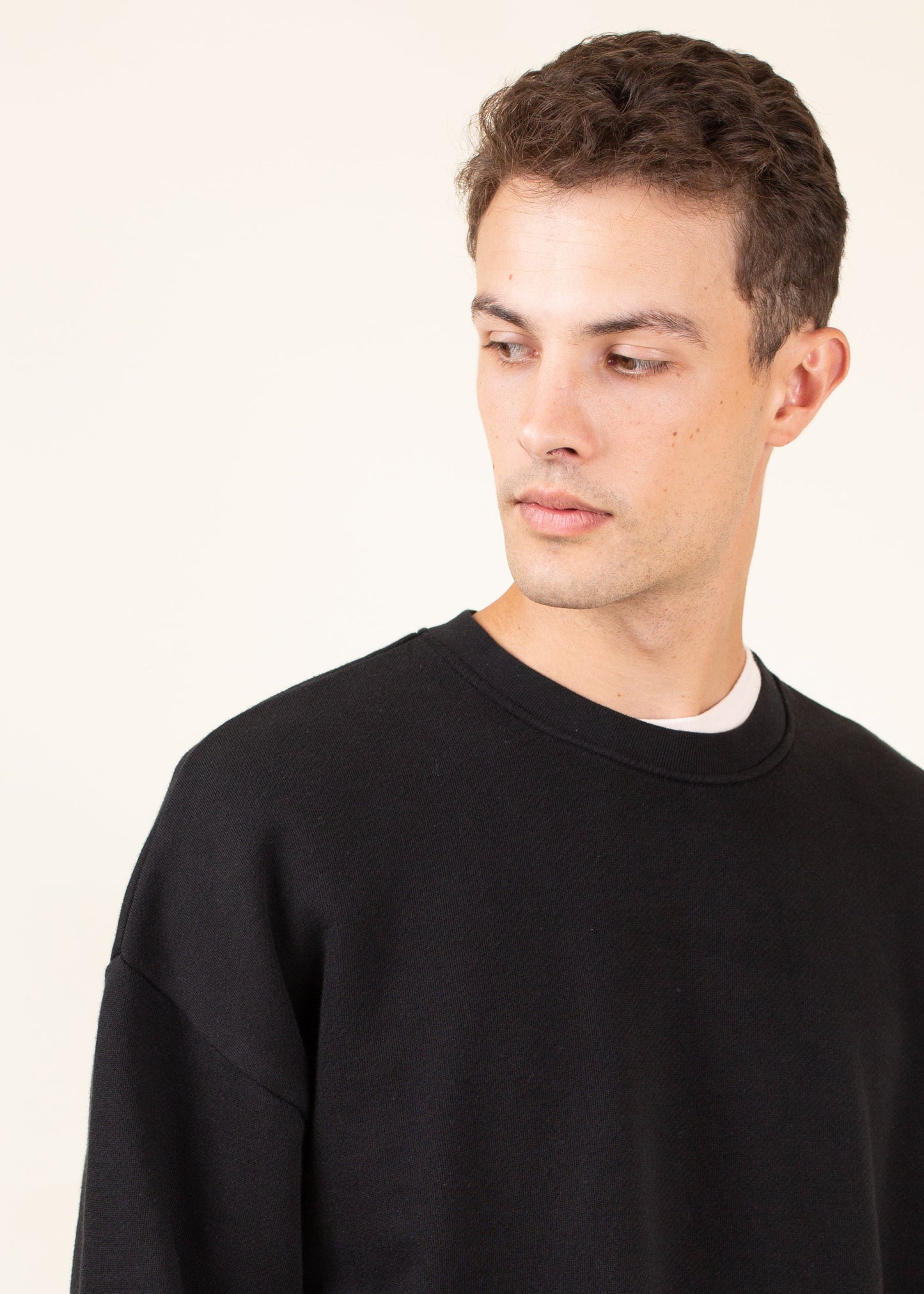 Man wearing a black crewneck sweatshirt, minimalist style, against a light background.