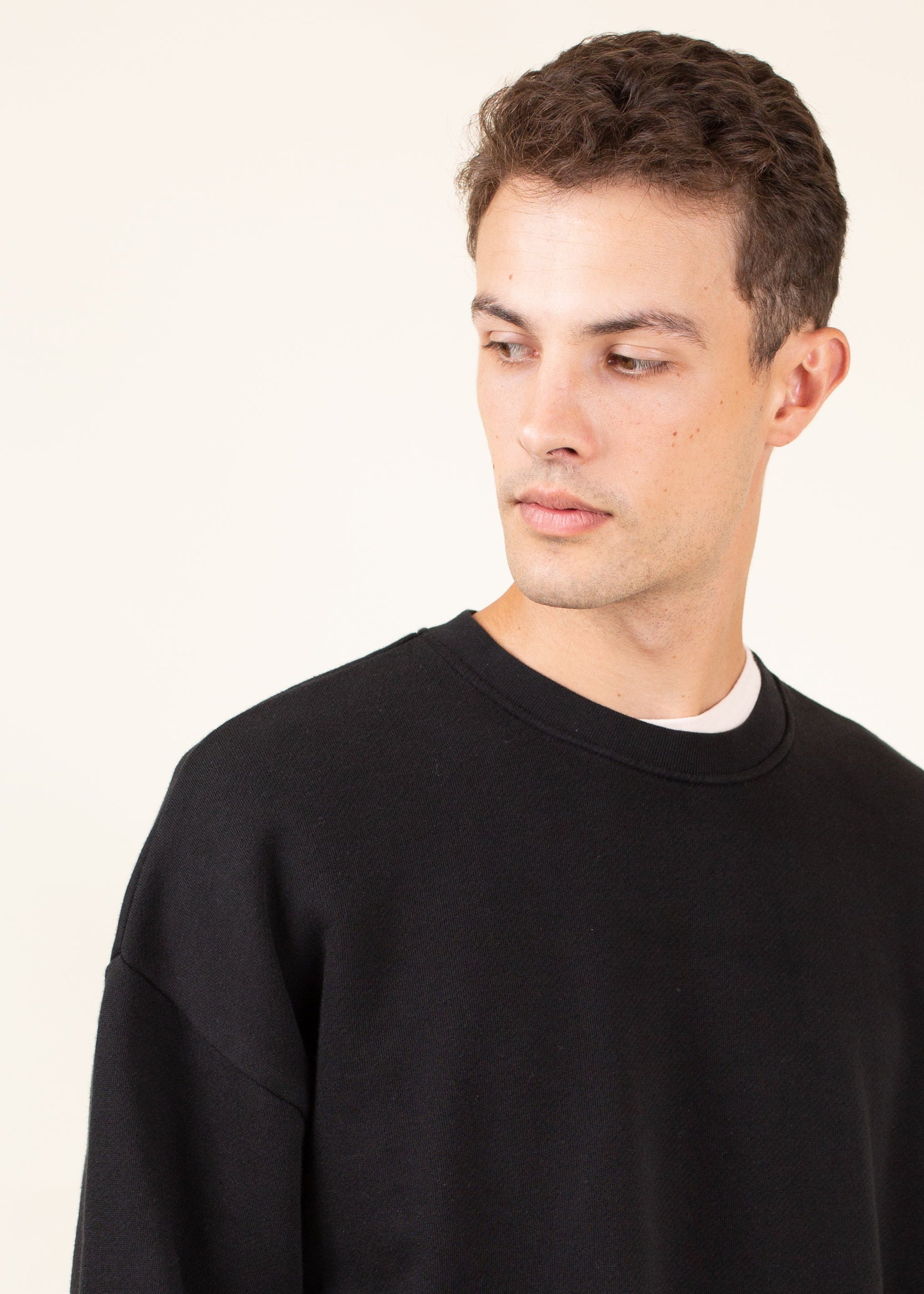 Man wearing a black crewneck sweatshirt, minimalist style, against a light background.