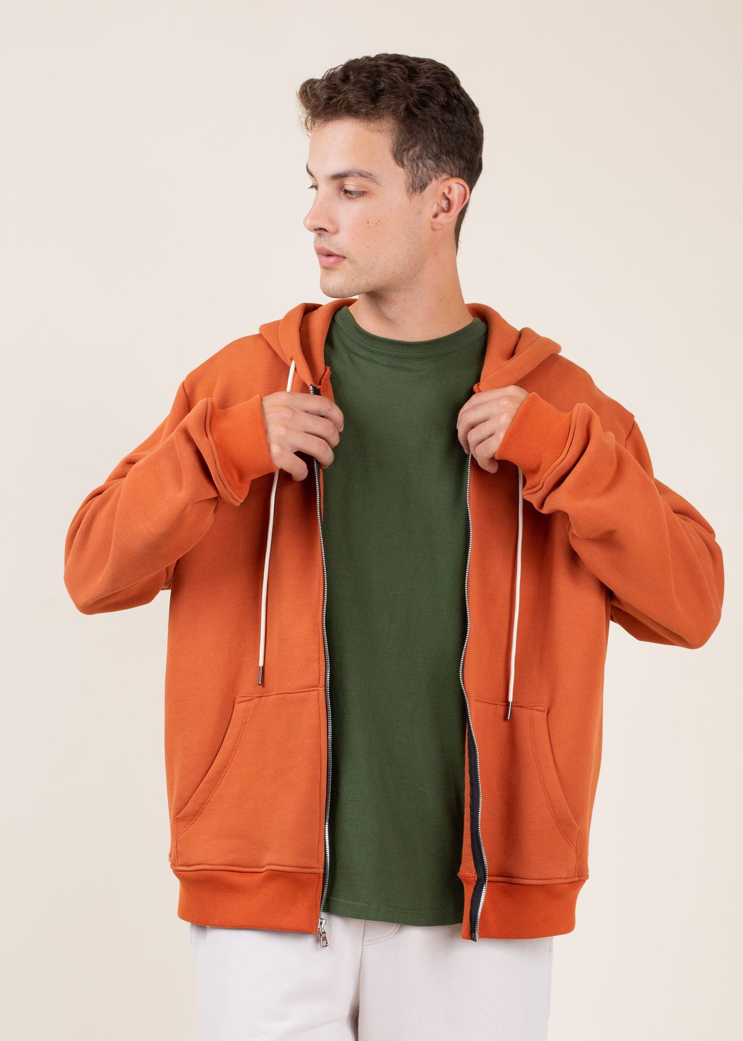 Man in orange zip hoodie and green shirt, stylish men's fashion, neutral background