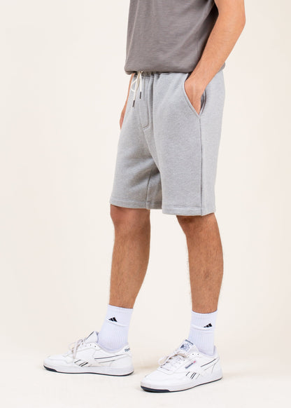 Man wearing grey athletic shorts, white Reebok sneakers, and white crew socks on neutral background