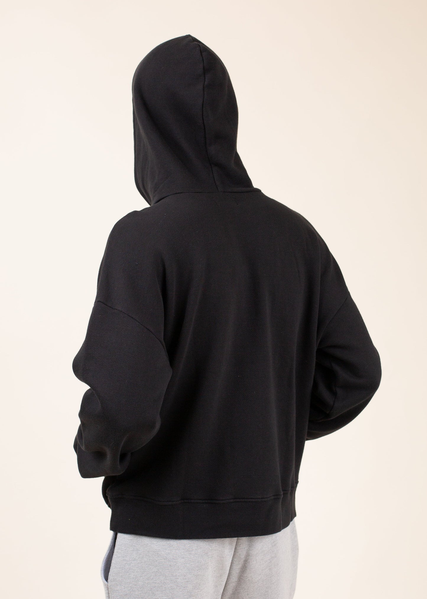 Man wearing black hoodie and gray sweatpants, back view, casual men's fashion on beige background