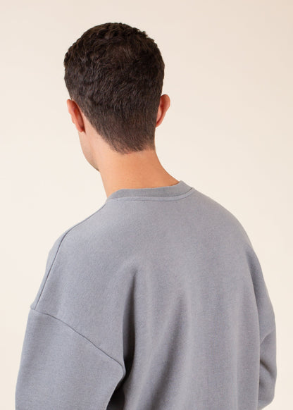 Man in a grey sweatshirt facing backward, short dark hair, minimal background, MANN fashion