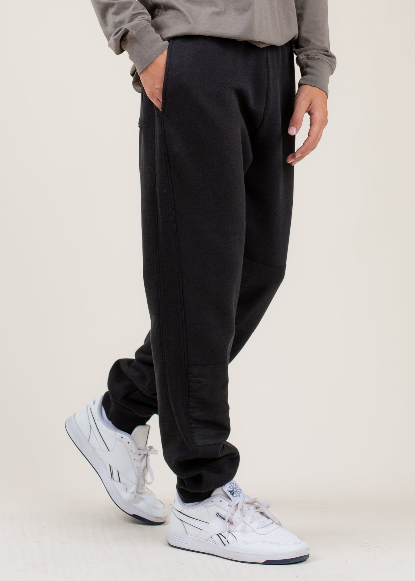 Men's black jogger pants with side pockets, styled with white Reebok sneakers from MANN.