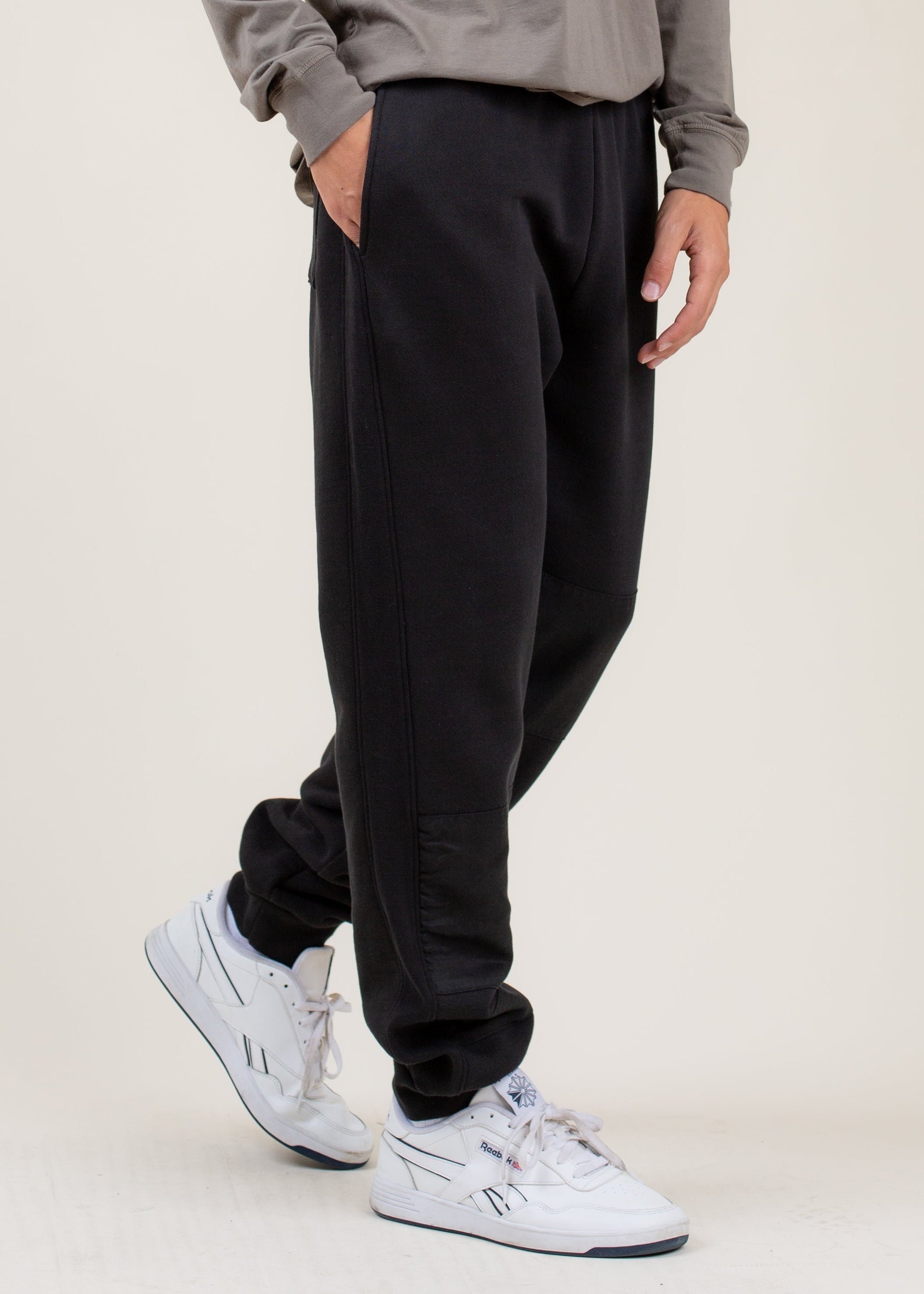 Men's black jogger pants with side pockets, styled with white Reebok sneakers from MANN.
