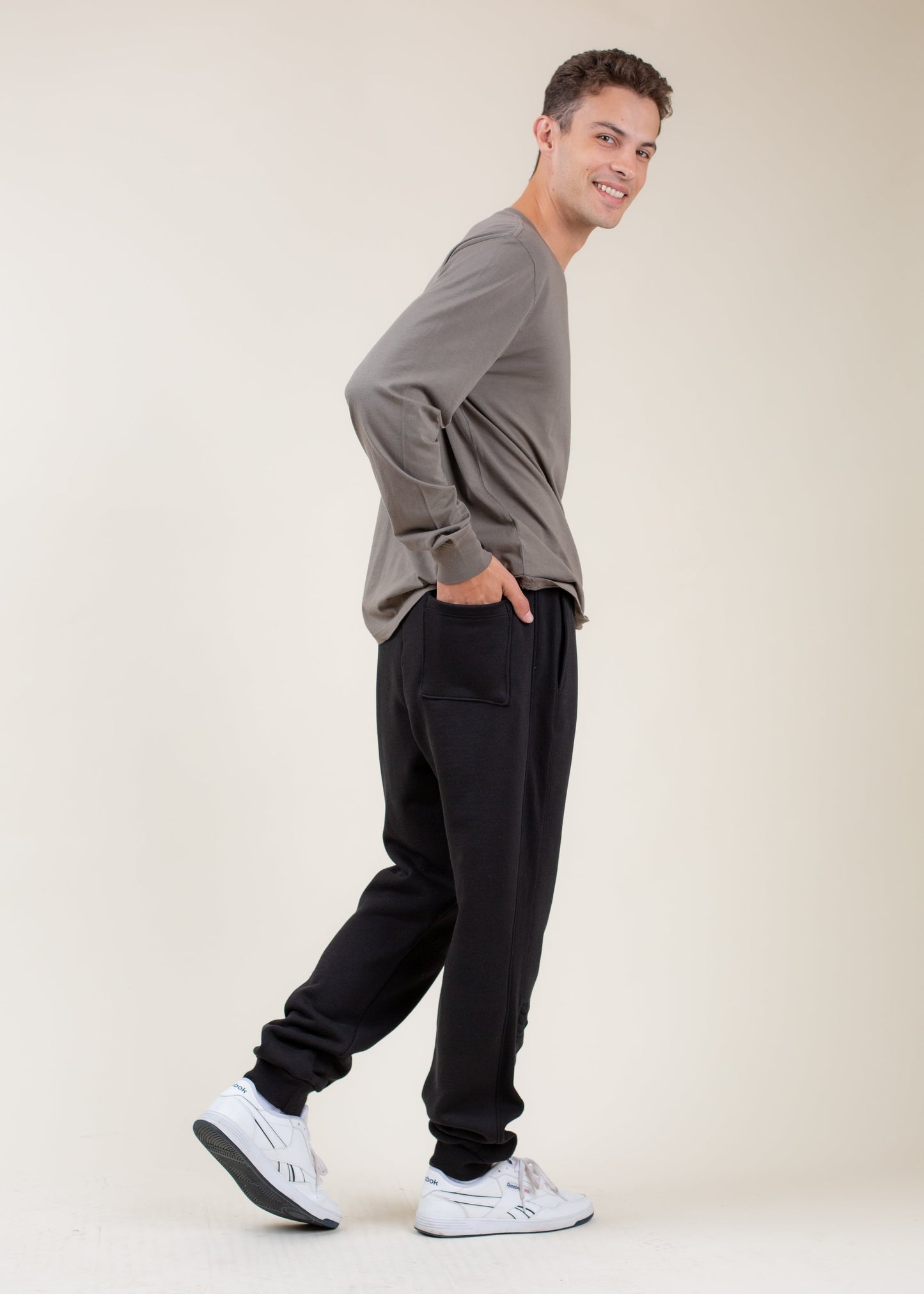 Smiling man in casual men’s fashion, gray long-sleeve shirt and black joggers, white sneakers