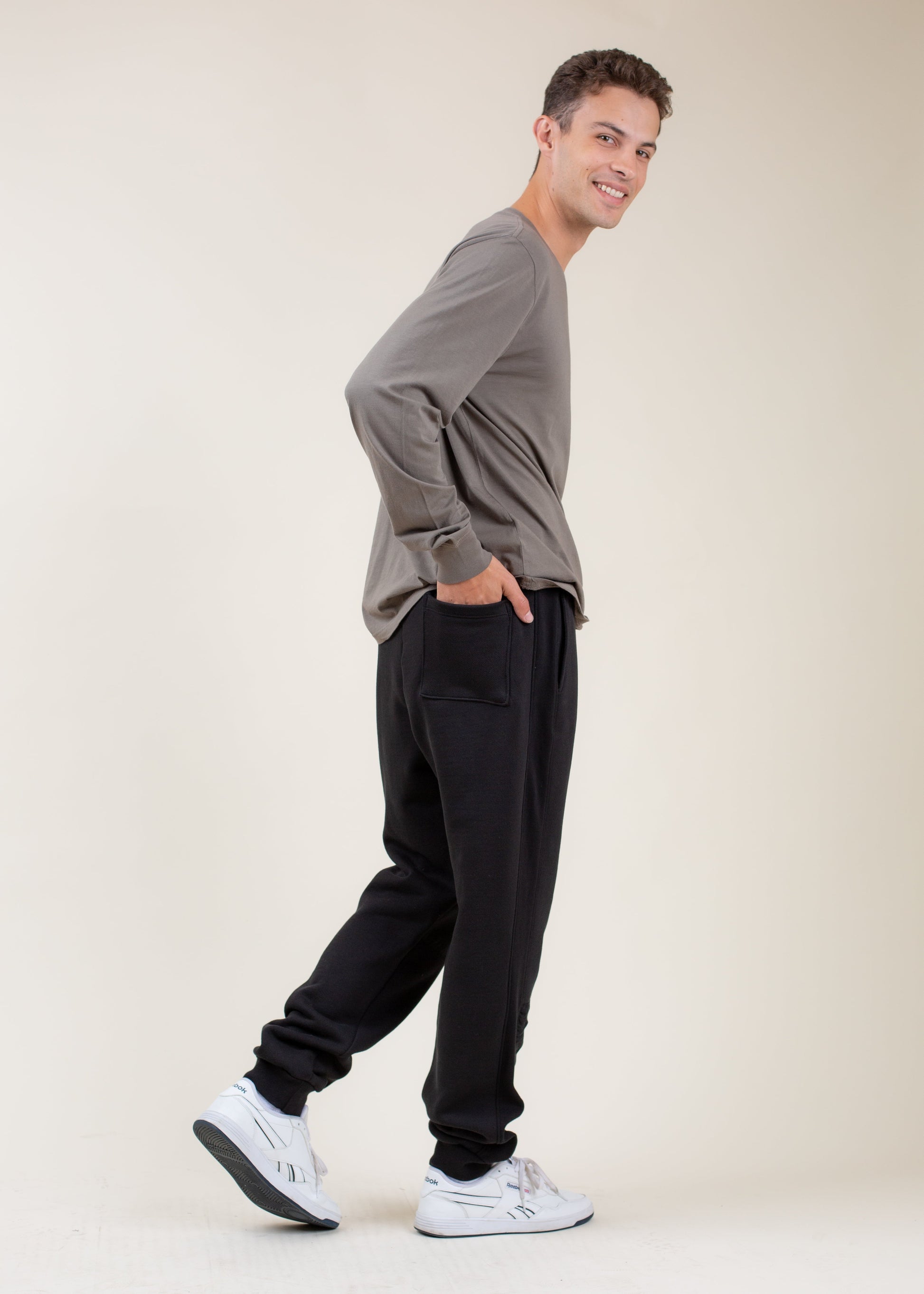 Smiling man in casual men’s fashion, gray long-sleeve shirt and black joggers, white sneakers