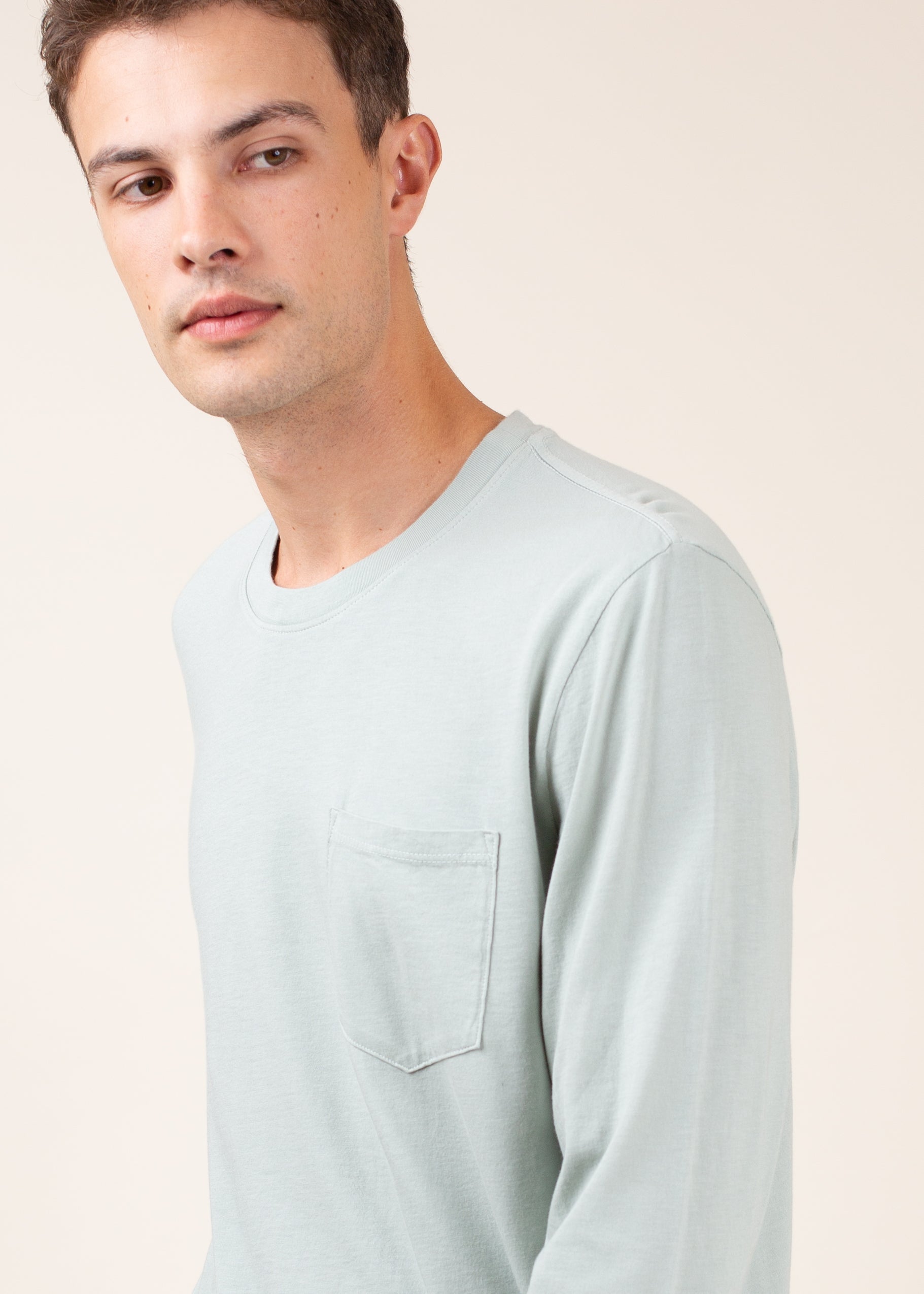 Man wearing light grey long sleeve crew neck shirt with chest pocket, neutral background