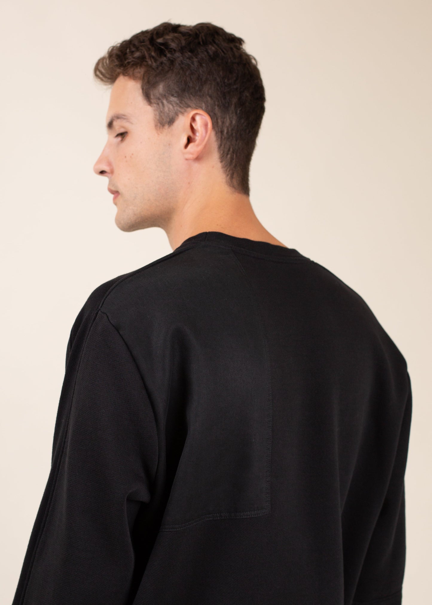 Man in black crewneck shirt, side view, minimalist fashion on beige background