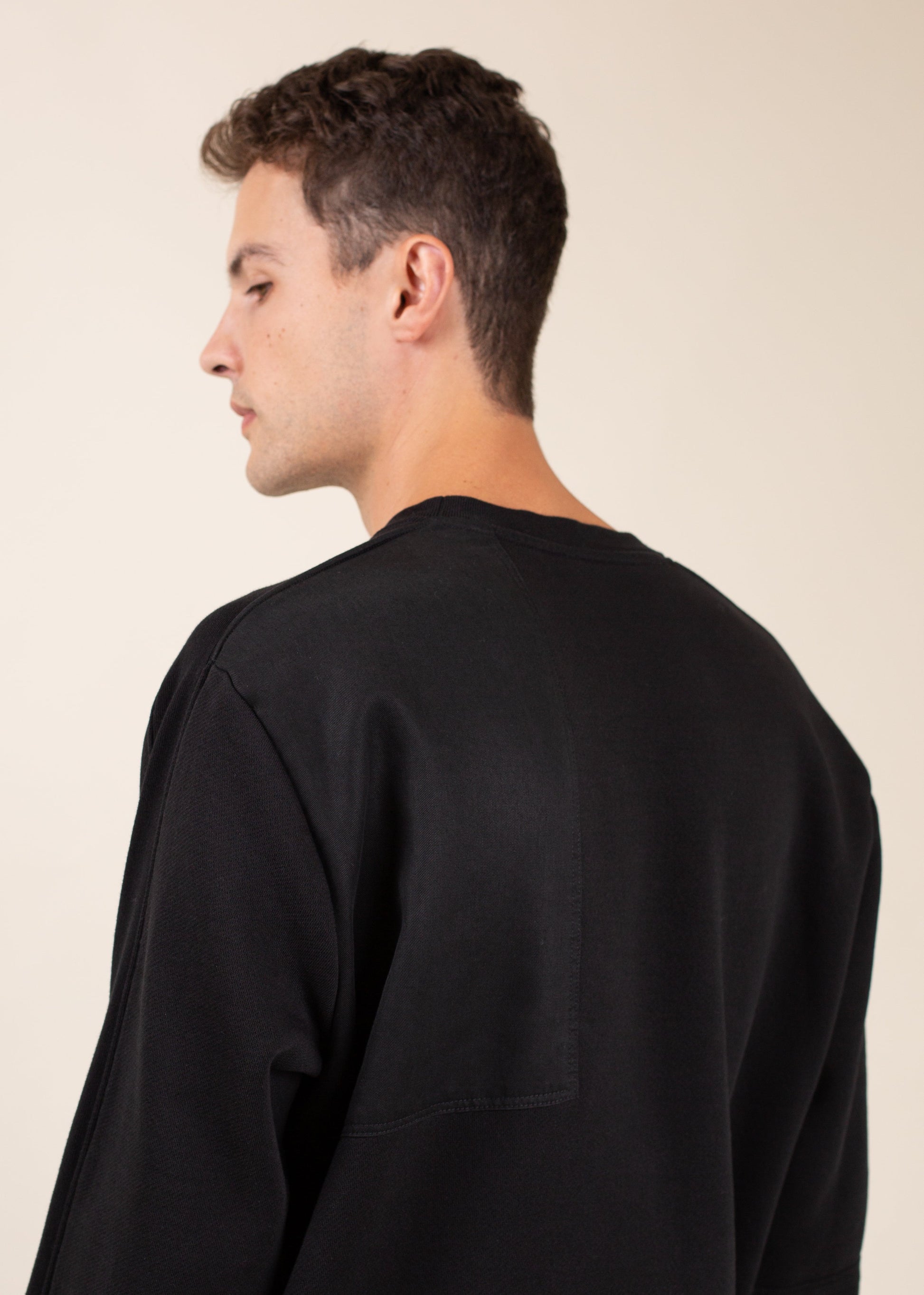 Man in black crewneck shirt, side view, minimalist fashion on beige background