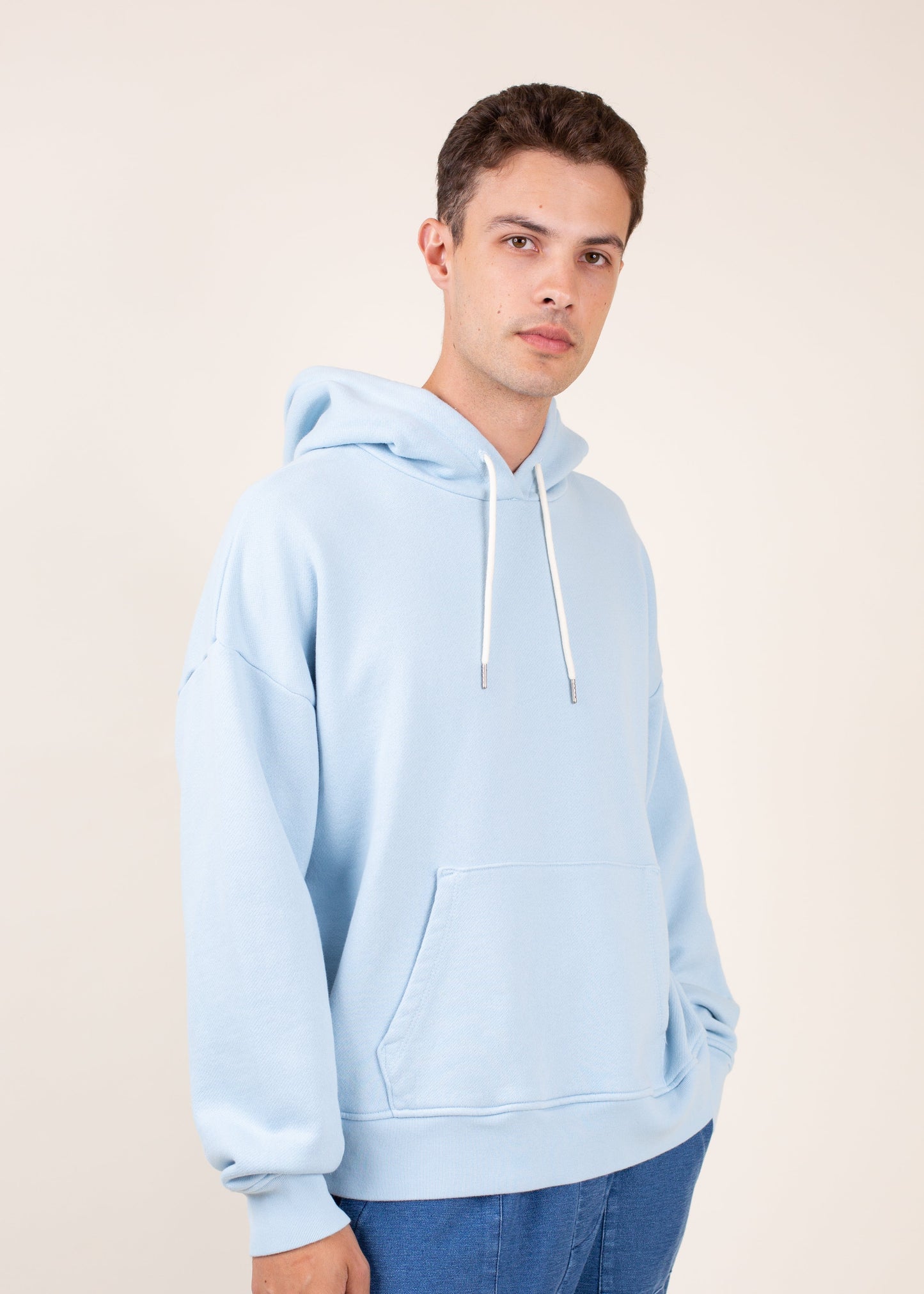 Man wearing light blue hoodie and jeans, casual men's fashion on neutral background