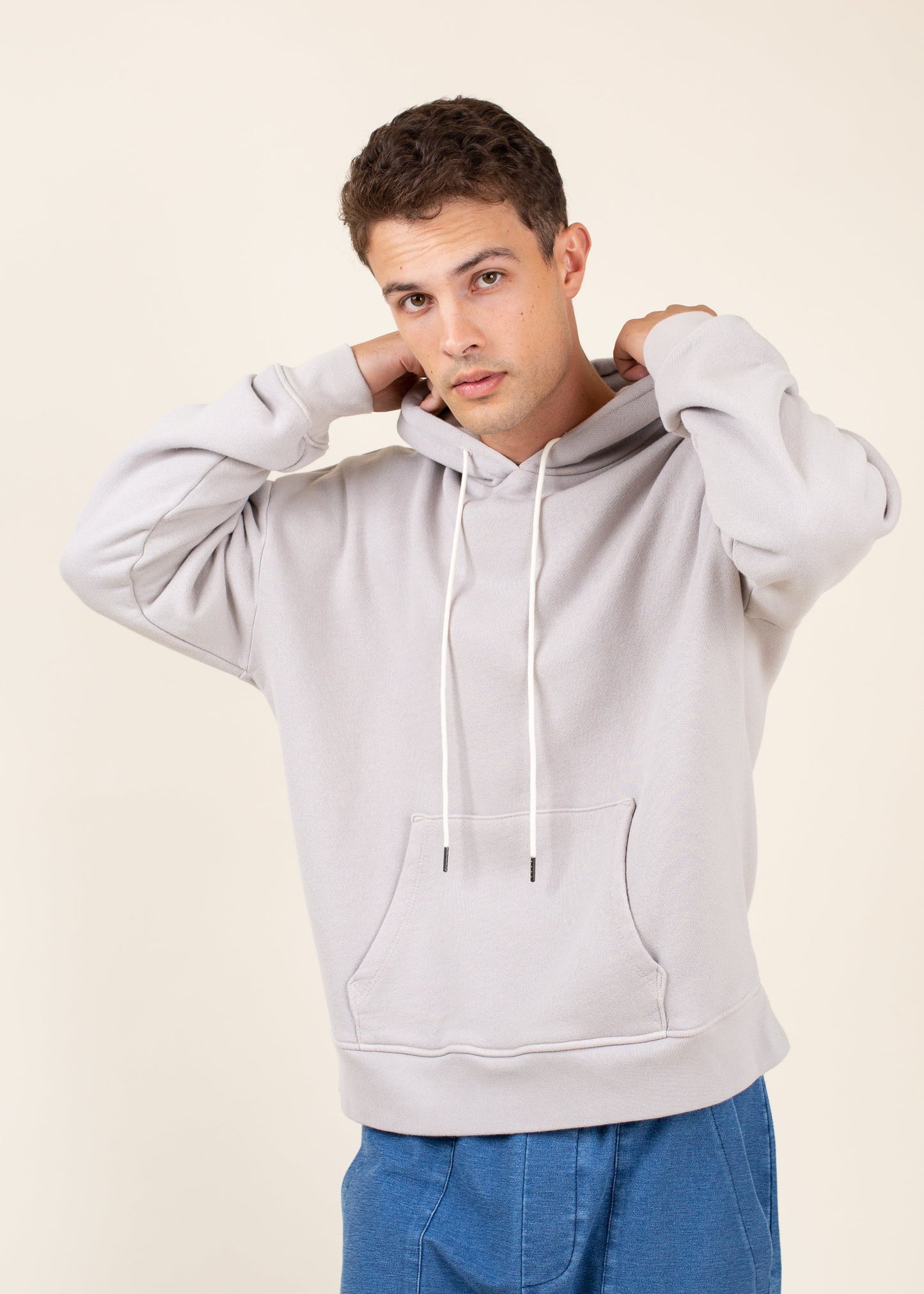 Man modeling light gray hoodie with drawstrings and blue pants, men's fashion lifestyle