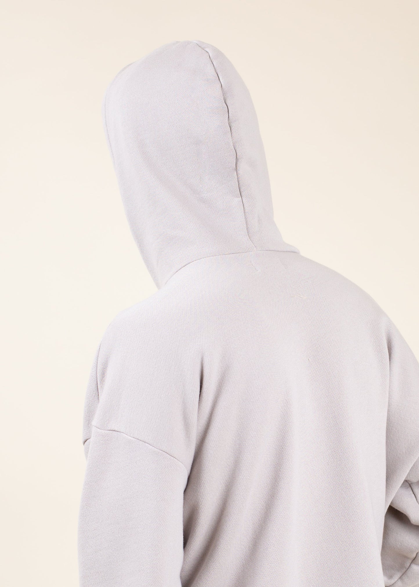Back view of a light grey men’s hoodie against a beige background, fashion apparel from Mann marketplace
