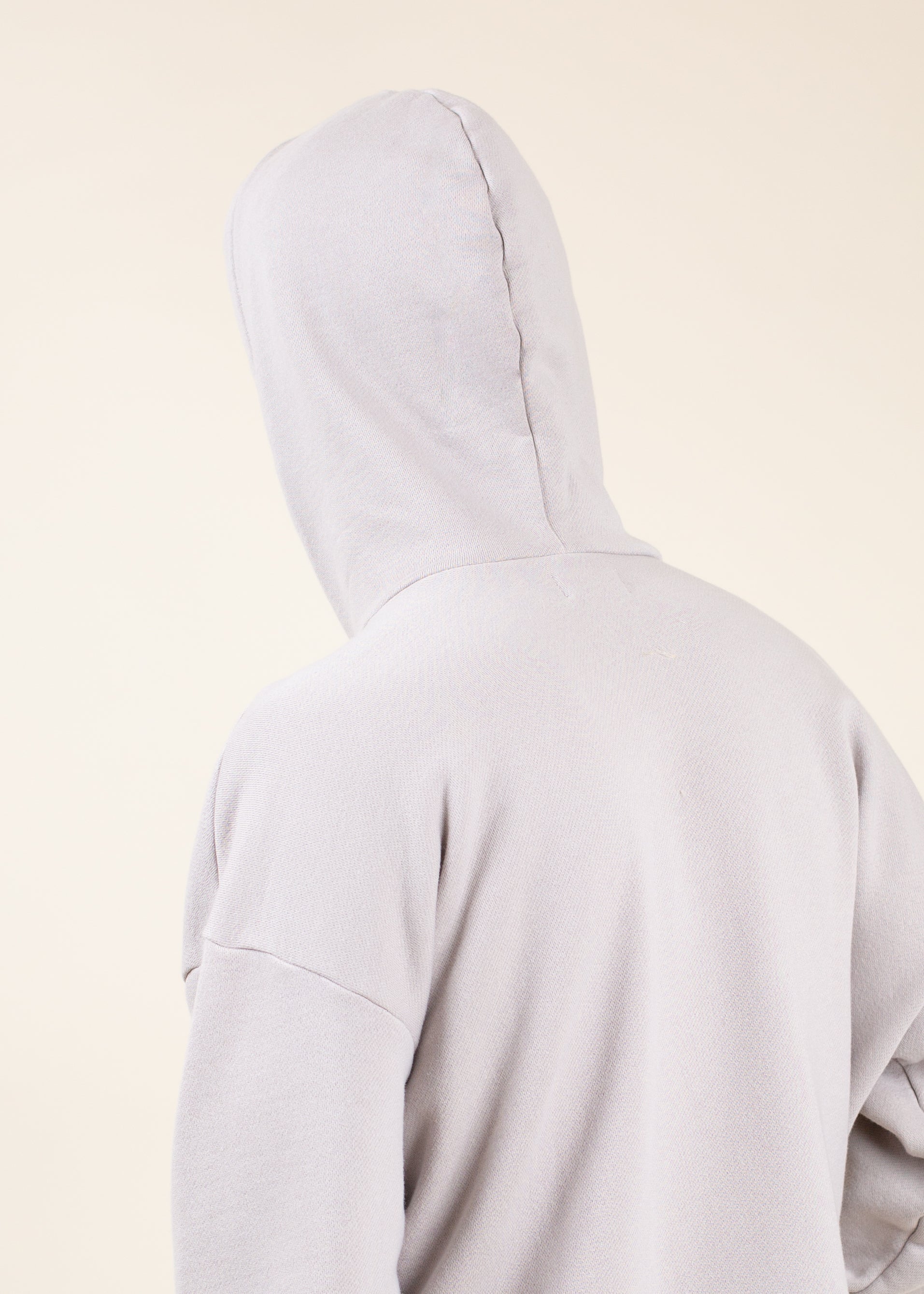 Back view of a light grey men’s hoodie against a beige background, fashion apparel from Mann marketplace