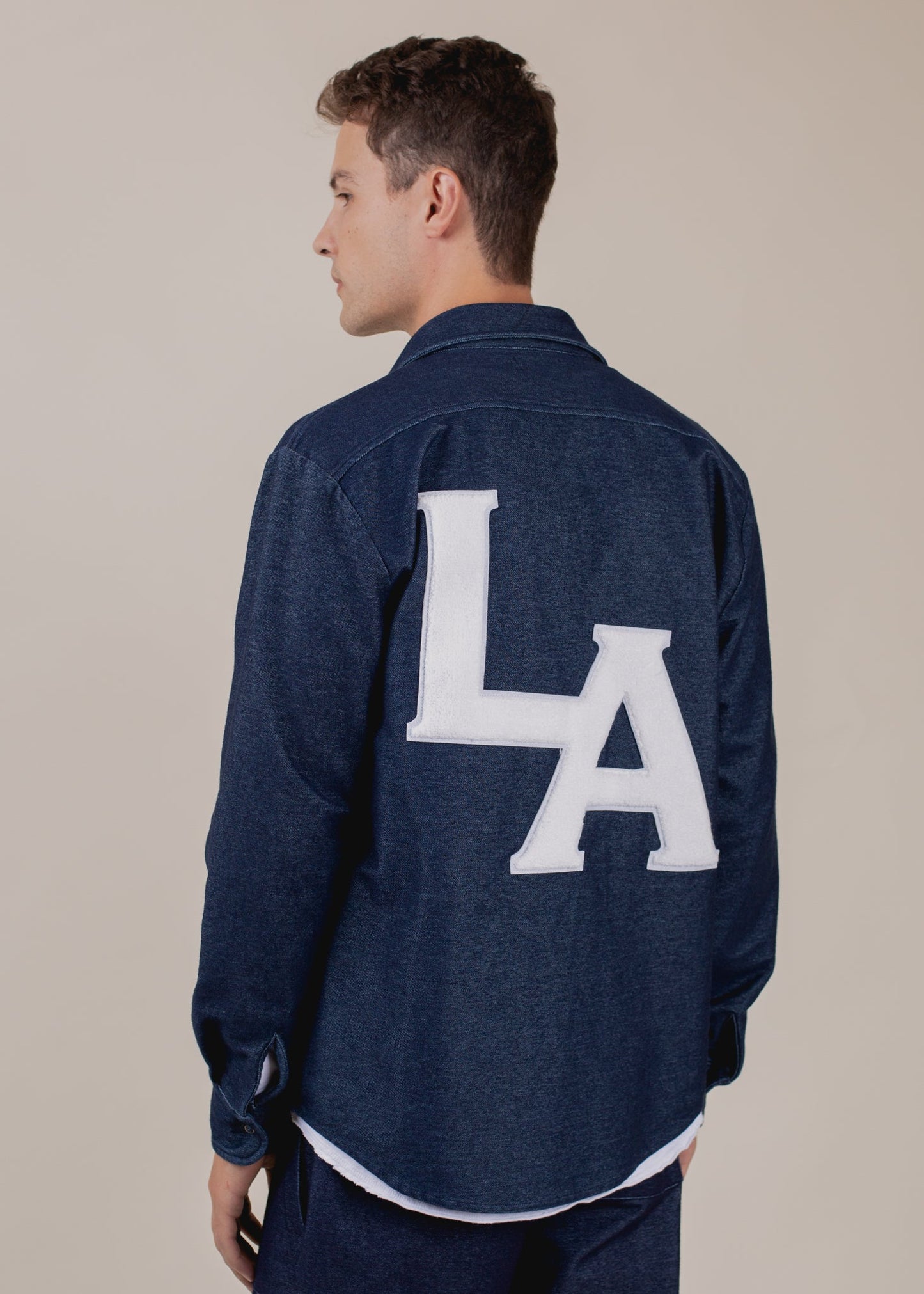 Man wearing indigo button-down shirt with large white LA letters on back, Mann menswear