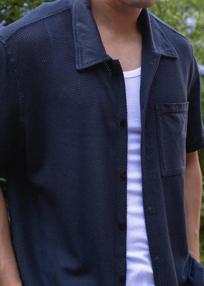Close-up of a man wearing a navy mesh button-down shirt over a white tank top outdoors