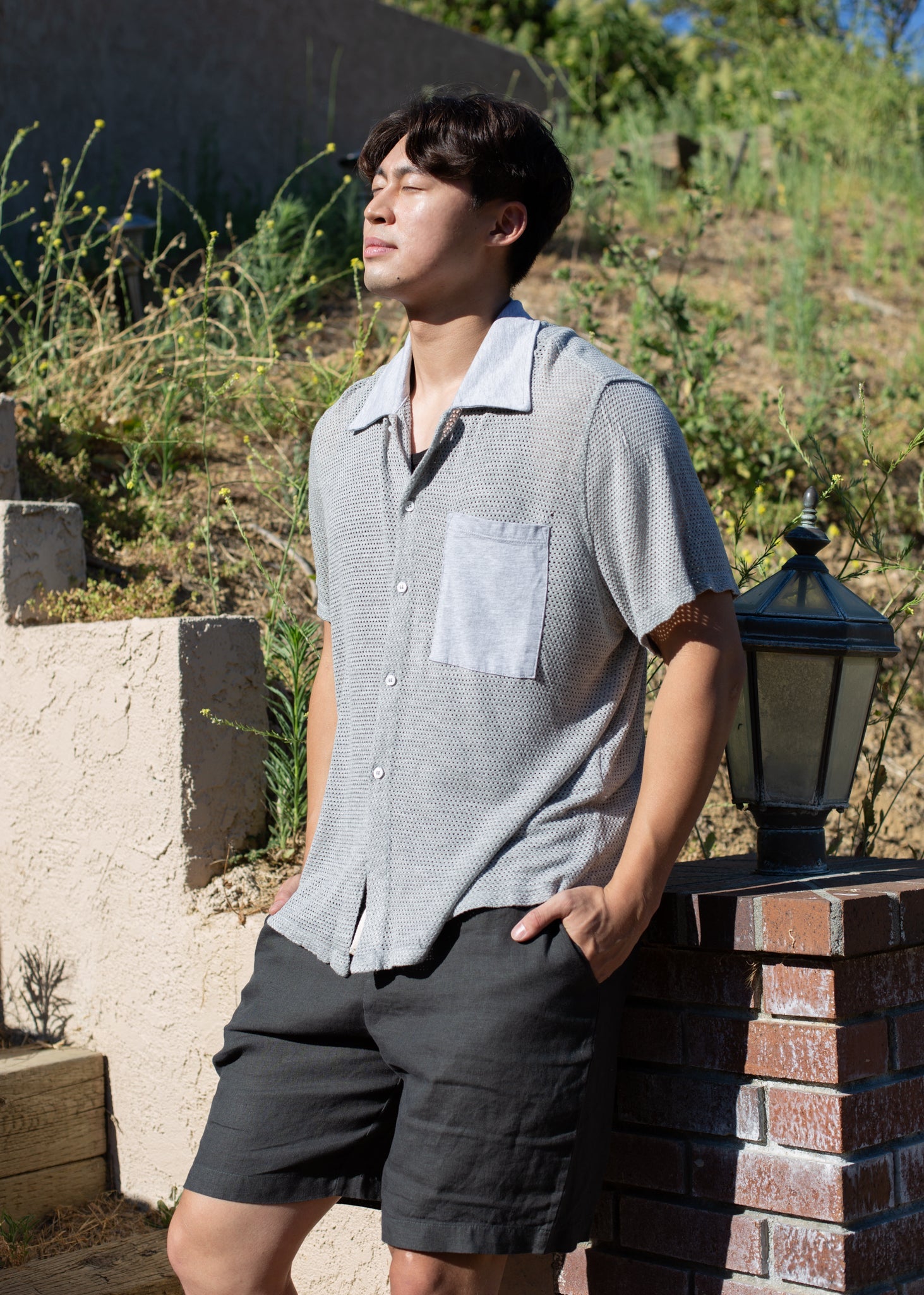 Man wearing a light grey mesh button-down shirt and black shorts outdoors in sunlight