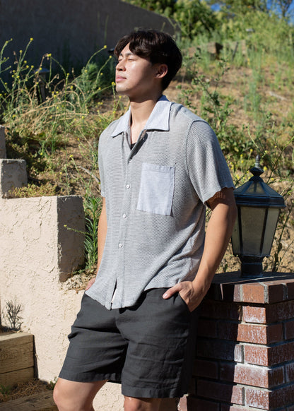 Man wearing a light grey mesh button-down shirt and black shorts outdoors in sunlight