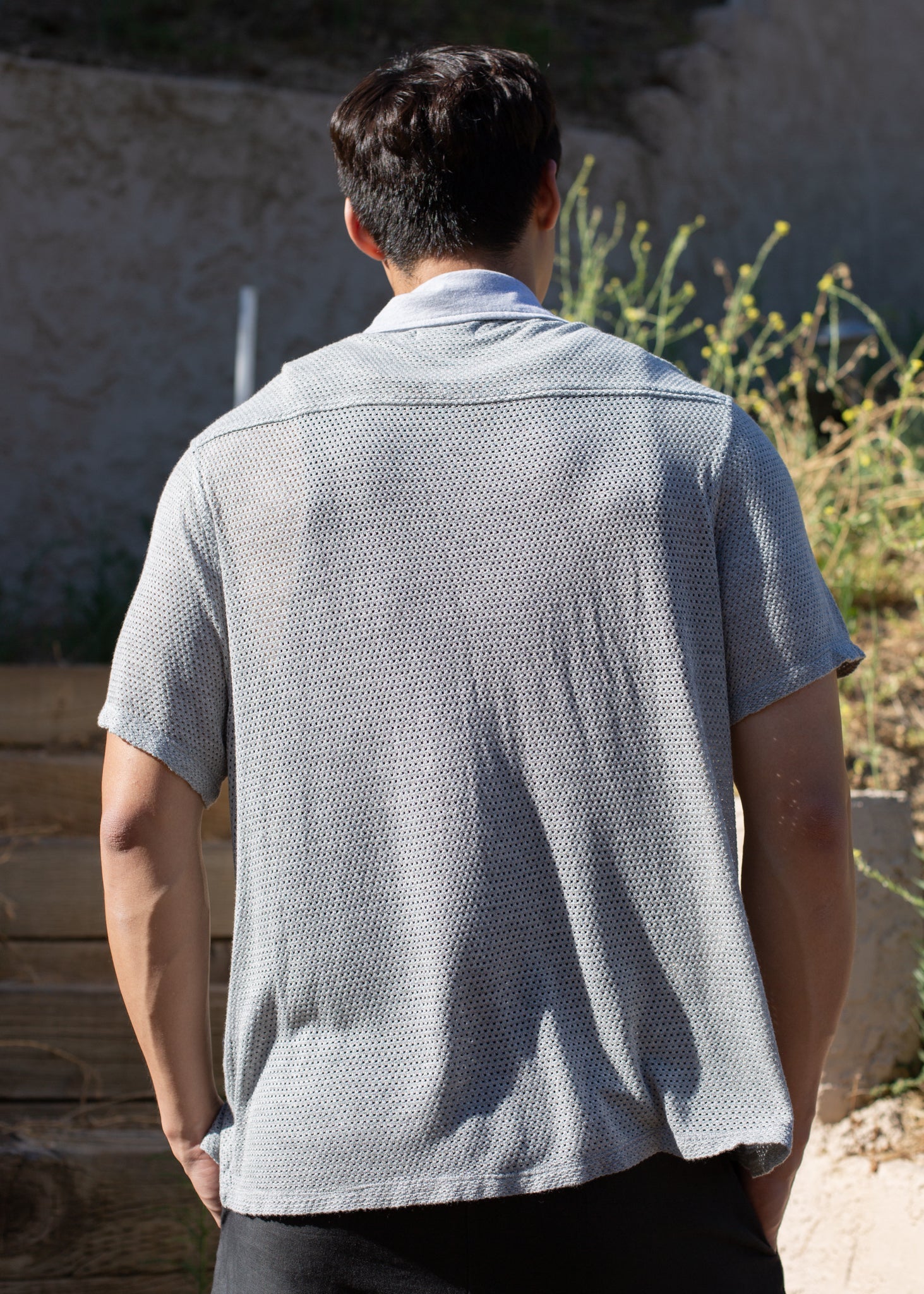 Man wearing a light grey mesh button-down shirt outdoors, shown from the back