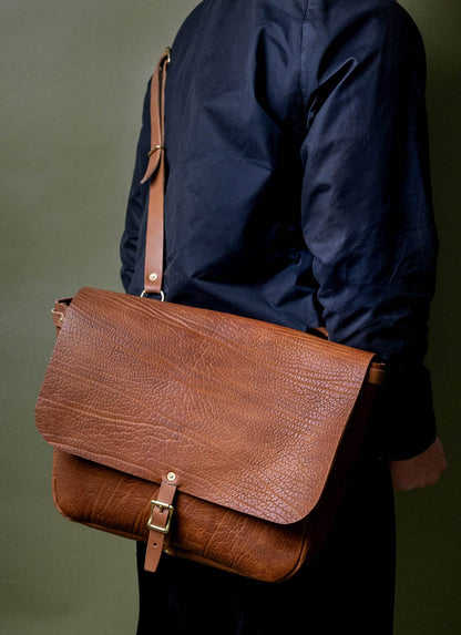 Man wearing a textured brown leather messenger bag with gold buckle, fashion accessory for men