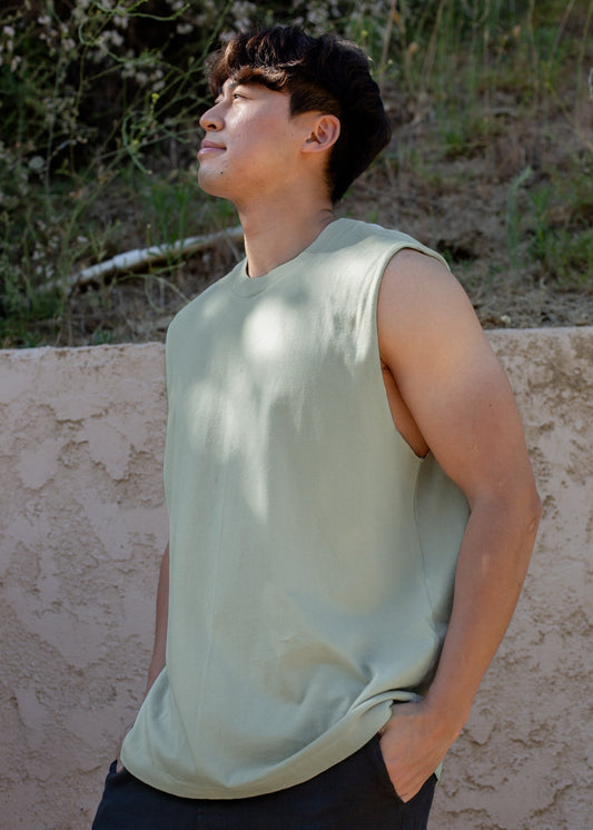 Man wearing sage green muscle tank top outdoors against textured wall, casual men’s fashion