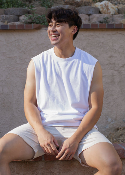 Smiling man wearing a white muscle tank and beige shorts, outdoor casual fashion for men
