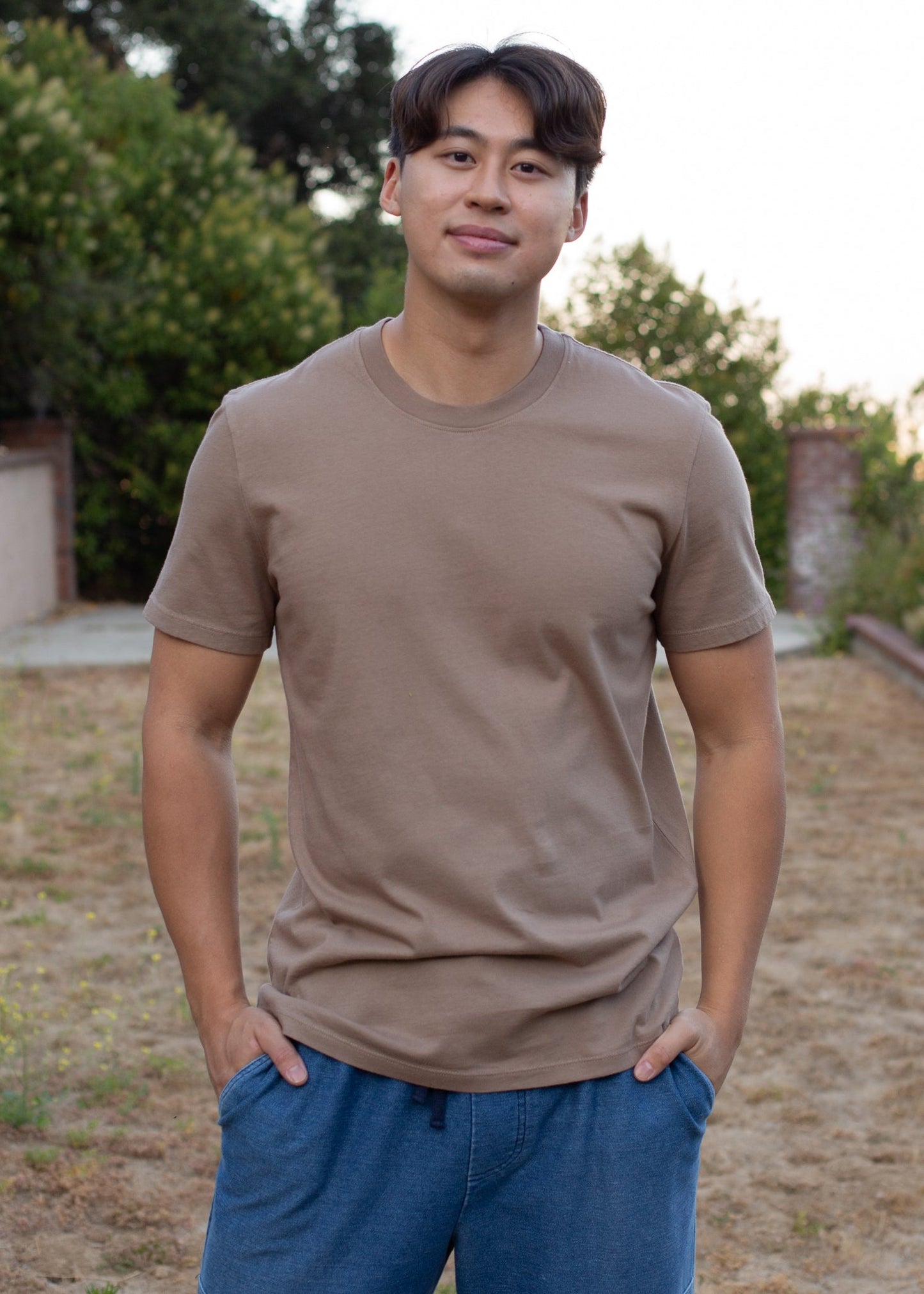 Man wearing organic mushroom brown basic tee and blue shorts outdoors