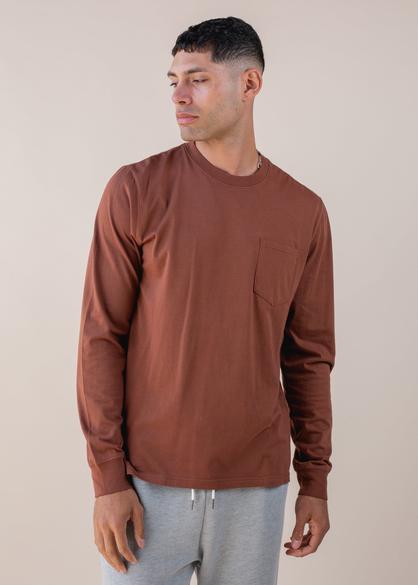 Man in brown long-sleeve shirt and grey joggers, stylish casual menswear on neutral background