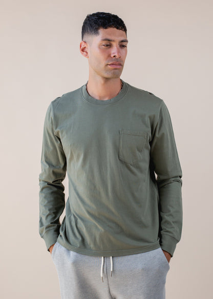 Man wearing olive green long sleeve pocket shirt and grey joggers, neutral background, MANN fashion
