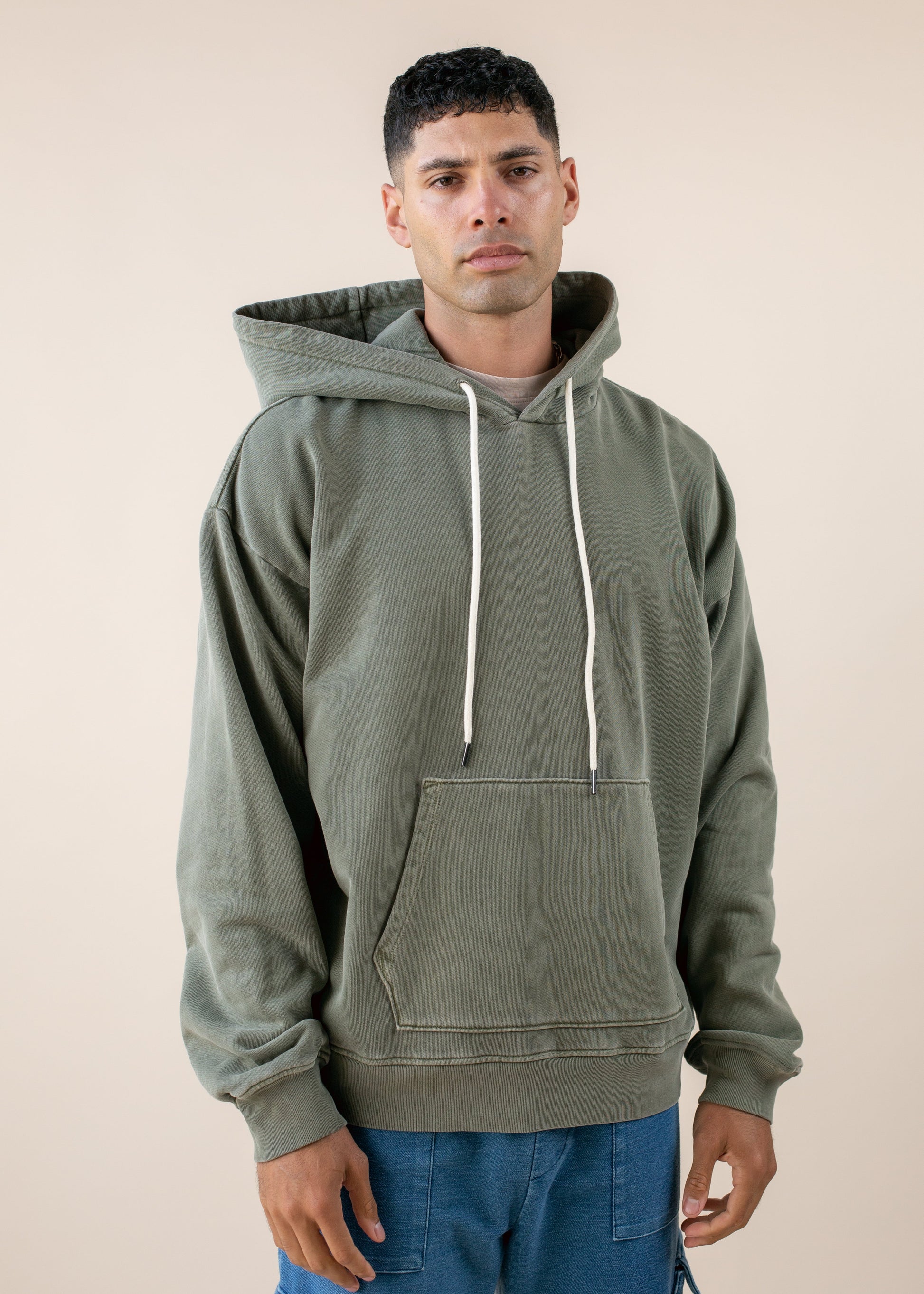 Man in an olive green hoodie and blue pants, modern men's fashion, neutral background