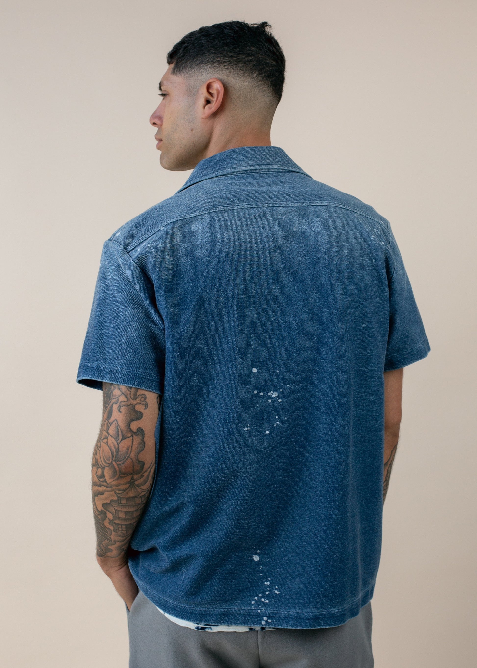 Man with tattooed arm wearing blue short sleeve shirt, back view, modern men's fashion