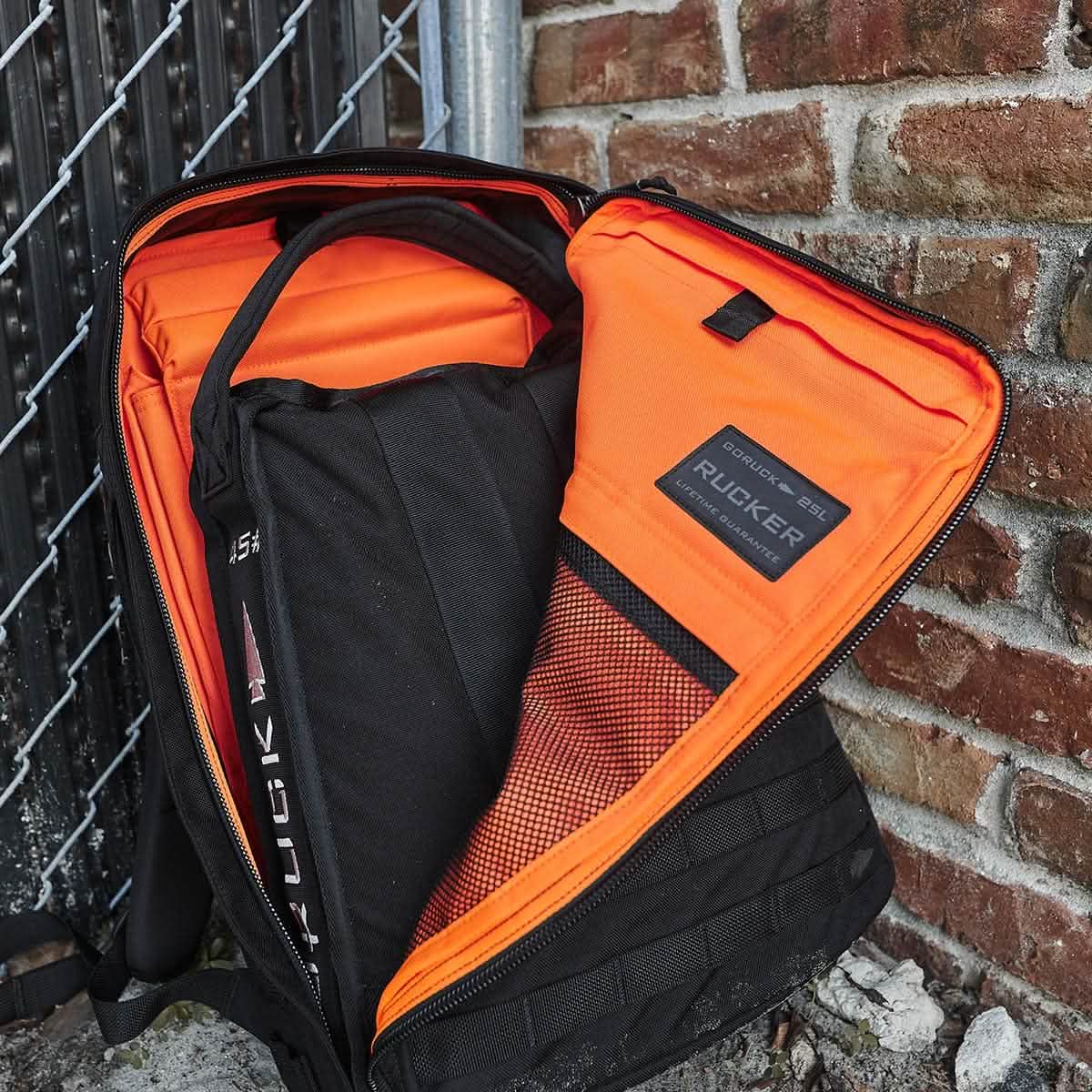 GORUCK Rucker 25L backpack with orange interior and training weight, placed by brick wall