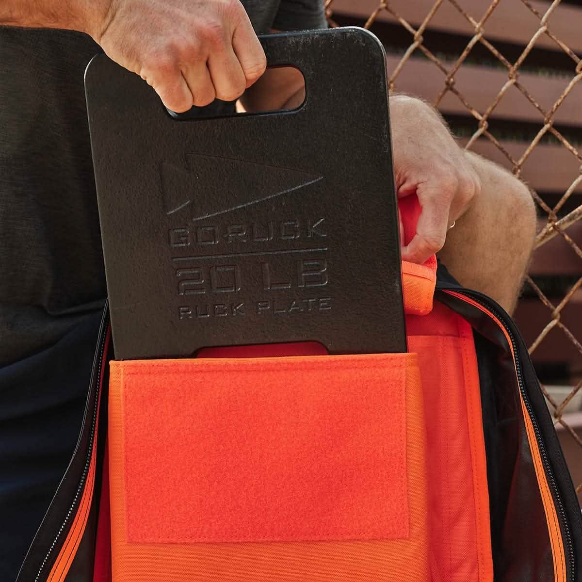 Man placing 20 lb GORUCK ruck plate into orange backpack, men's fitness gear