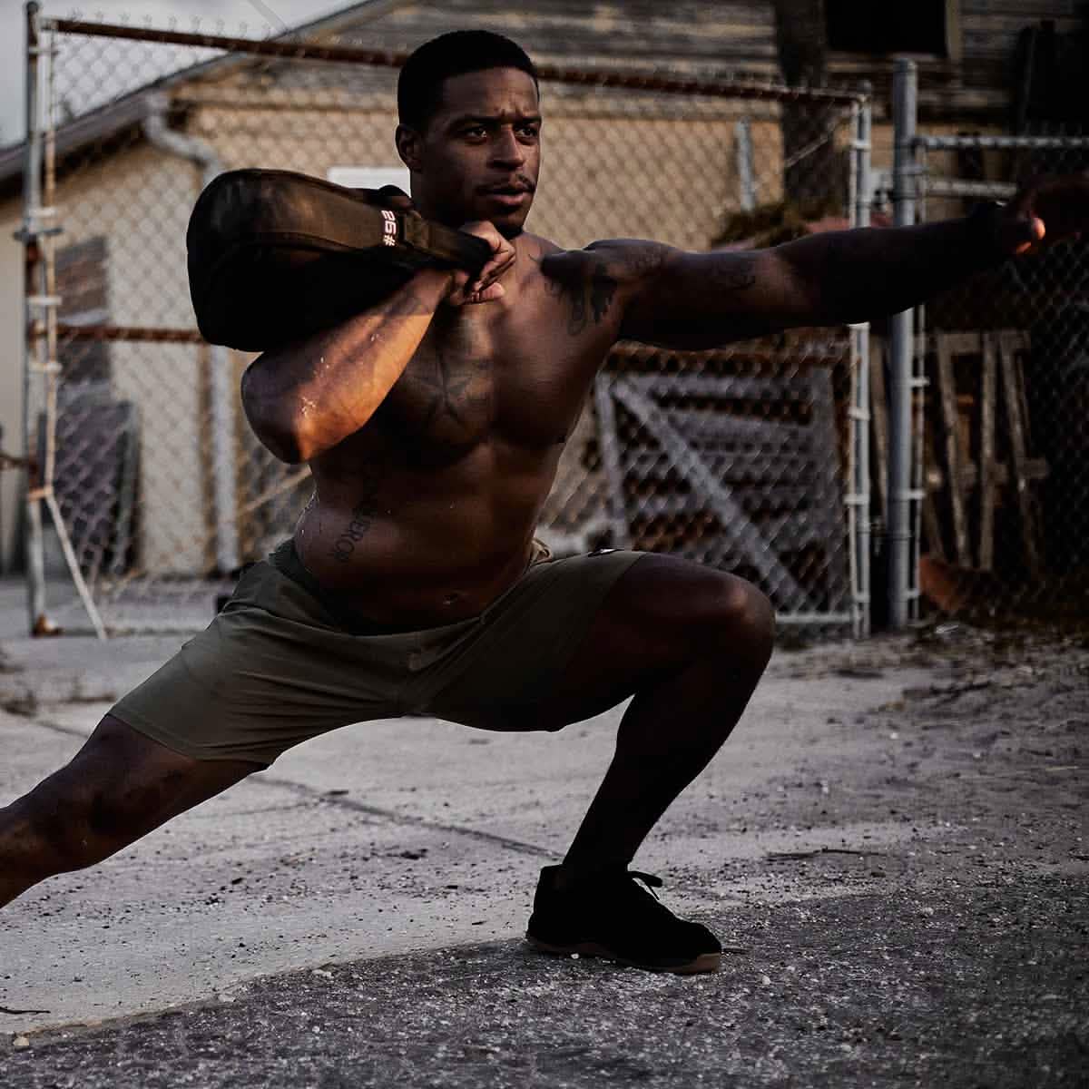 Athletic man training outdoors with weighted sandbag, showcasing men's fitness lifestyle.