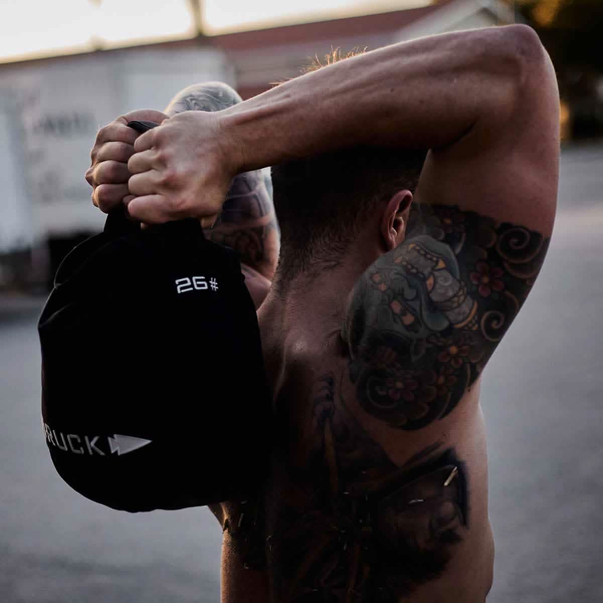 Tattooed man lifting 26 lb sandbag outdoors, fitness and active lifestyle for men