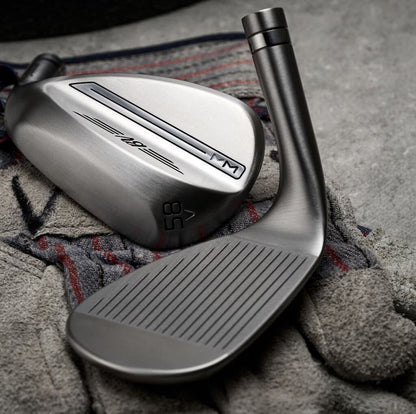 Close-up of two sleek golf wedges with brushed metal finish on a towel, men's lifestyle gear.