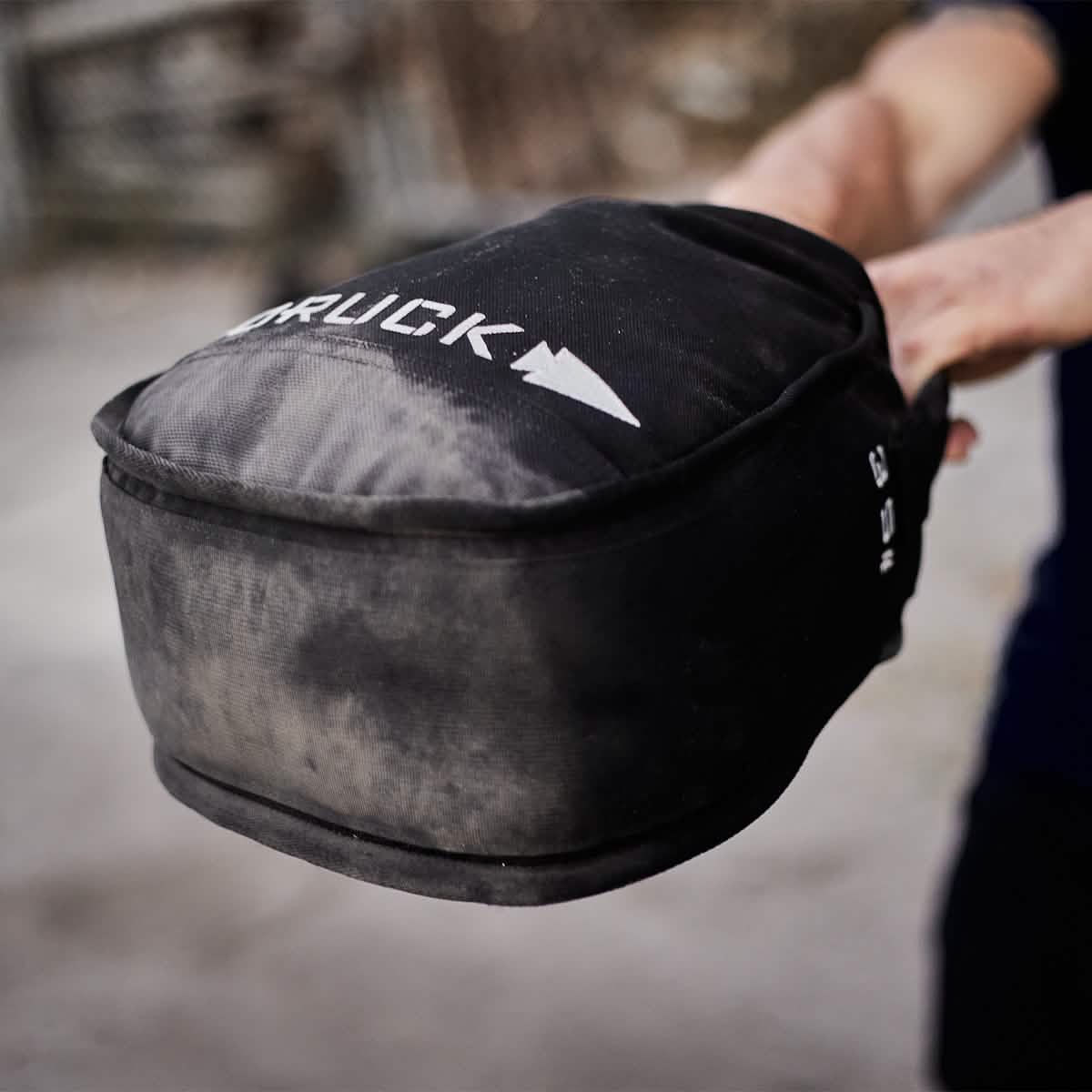 Close-up of a man holding a black GORUCK training sandbag outdoors, fitness gear for men