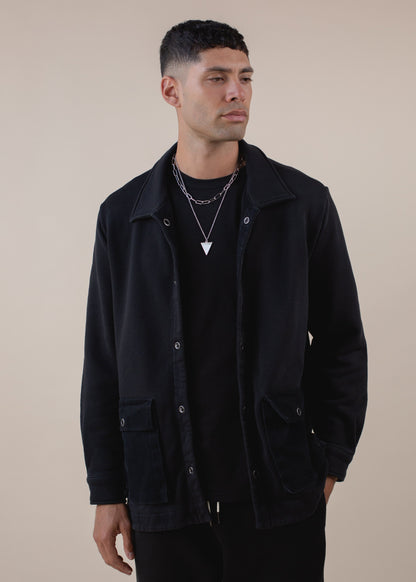 Man wearing black worker's jacket and silver necklace, minimalist fashion for men